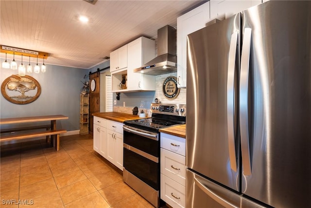 kitchen featuring wood counters, white cabinets, stainless steel appliances, a barn door, and wall chimney exhaust hood