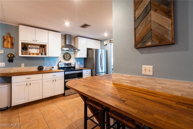 kitchen with light tile patterned flooring, butcher block countertops, white cabinetry, stainless steel appliances, and wall chimney exhaust hood