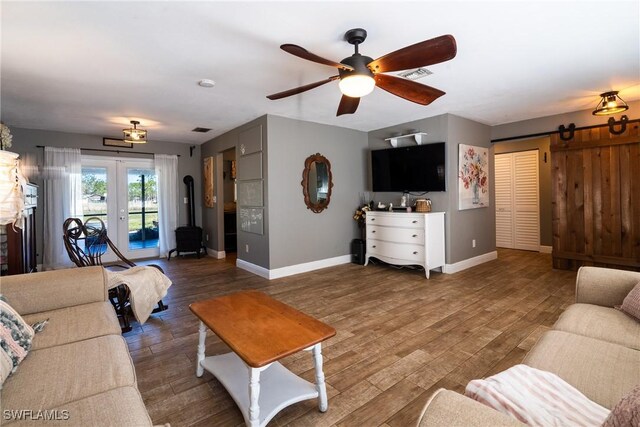 living room with dark wood-type flooring, french doors, ceiling fan, and a barn door