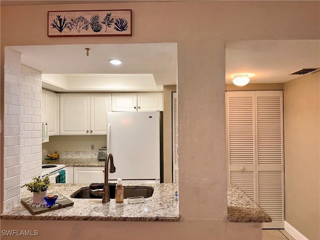 kitchen with light stone countertops, white appliances, visible vents, and a sink