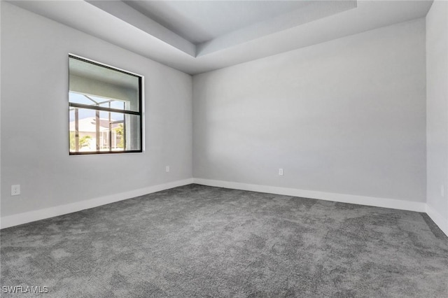 carpeted spare room featuring baseboards and a raised ceiling