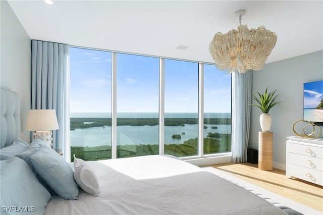 bedroom featuring multiple windows, a notable chandelier, wood-type flooring, and a water view