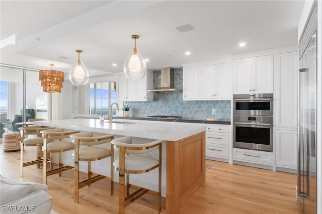 kitchen featuring wall chimney exhaust hood, a center island with sink, and white cabinets