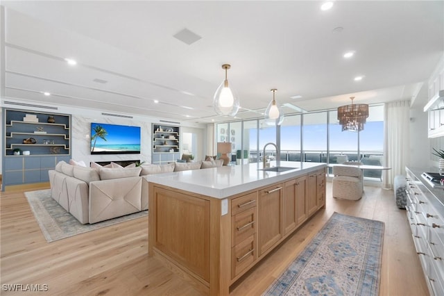 kitchen featuring an island with sink, sink, light hardwood / wood-style flooring, and decorative light fixtures