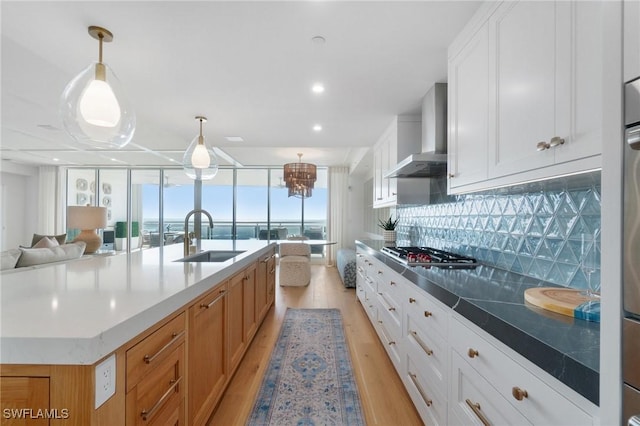 kitchen featuring a spacious island, sink, decorative light fixtures, wall chimney range hood, and white cabinets