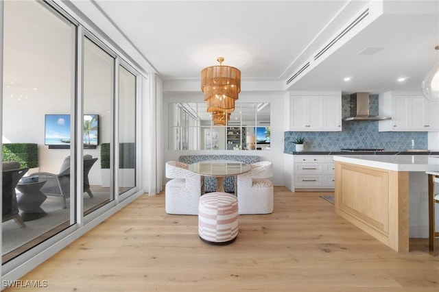 kitchen featuring white cabinetry, pendant lighting, light hardwood / wood-style flooring, and wall chimney range hood