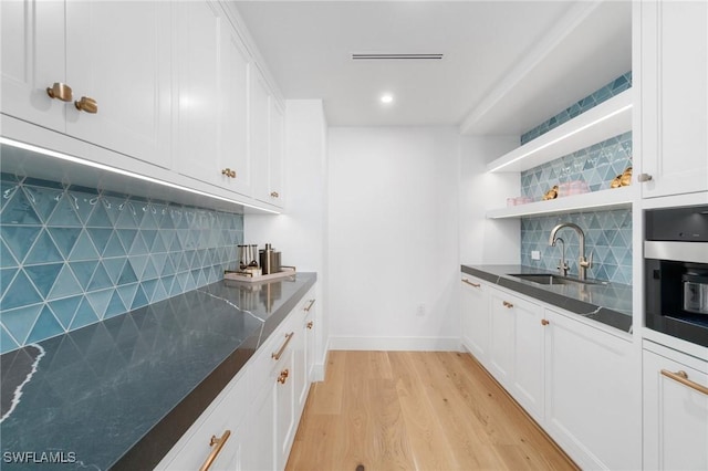 bar with sink, stainless steel oven, light wood-type flooring, white cabinets, and backsplash