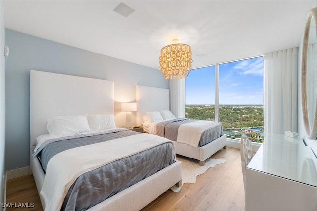 bedroom featuring an inviting chandelier, light hardwood / wood-style floors, and a wall of windows