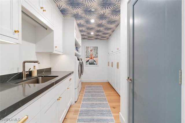 kitchen with sink, light wood-type flooring, dark stone countertops, washer / clothes dryer, and white cabinets