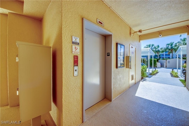 corridor with elevator, light carpet, and a textured ceiling