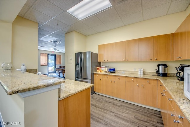 kitchen featuring stainless steel fridge, light hardwood / wood-style floors, kitchen peninsula, light stone countertops, and a drop ceiling