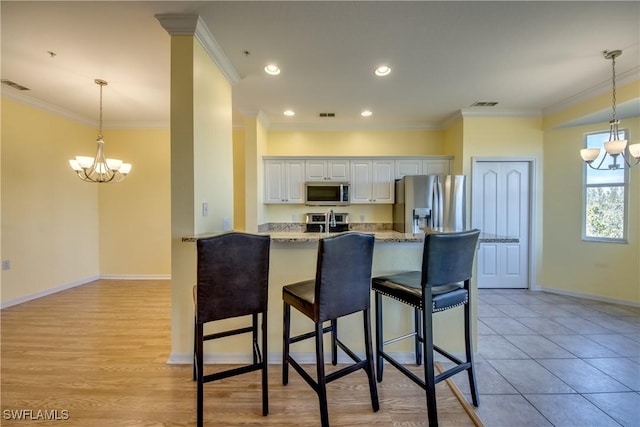 kitchen featuring stainless steel appliances, light stone countertops, white cabinets, kitchen peninsula, and a chandelier