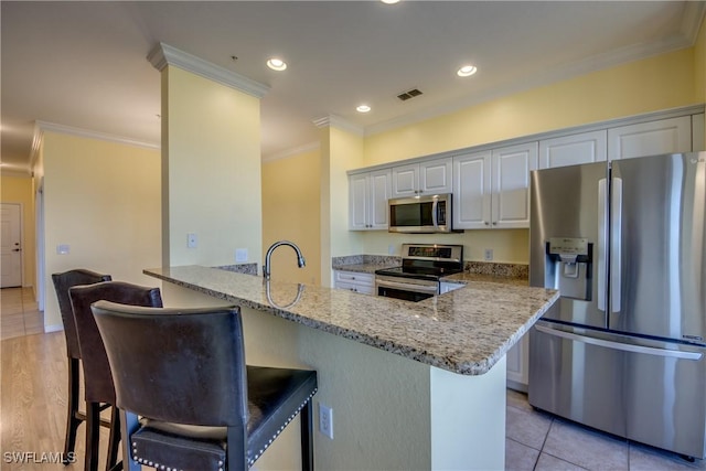 kitchen with a breakfast bar area, white cabinetry, stainless steel appliances, light stone counters, and kitchen peninsula