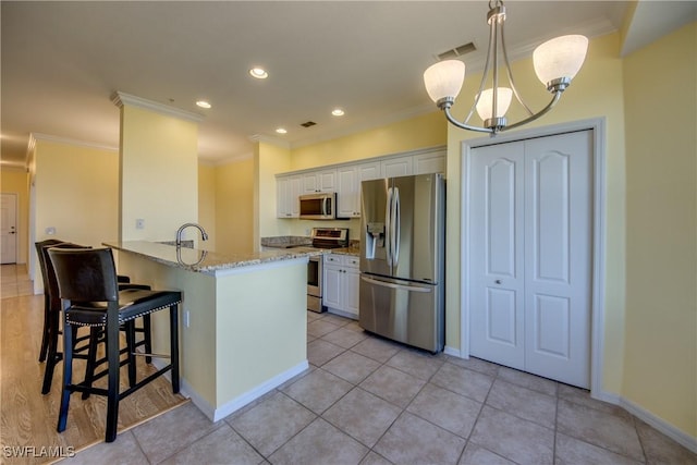 kitchen featuring white cabinetry, hanging light fixtures, ornamental molding, light stone counters, and stainless steel appliances