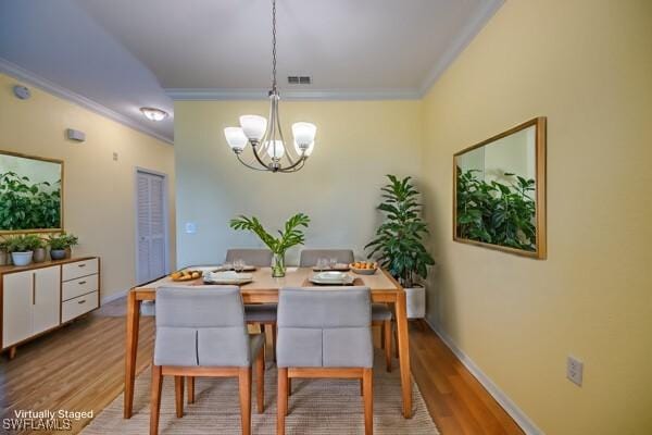 dining space with ornamental molding, a chandelier, and light hardwood / wood-style flooring