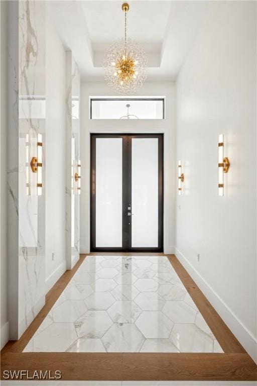 foyer with french doors, an inviting chandelier, and a tray ceiling