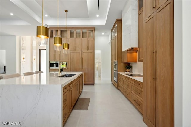 kitchen featuring sink, a tray ceiling, a center island with sink, black electric cooktop, and decorative light fixtures