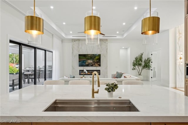 kitchen with a kitchen island with sink, decorative light fixtures, light stone countertops, and a premium fireplace