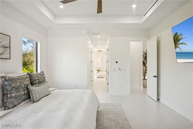 bedroom featuring a water view, ensuite bath, and a raised ceiling