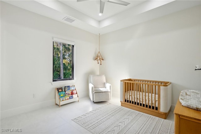 bedroom with a nursery area, ceiling fan, and a raised ceiling