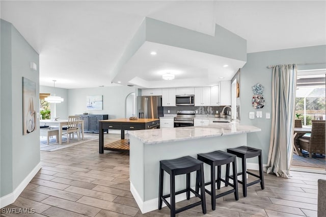 kitchen featuring appliances with stainless steel finishes, a wealth of natural light, kitchen peninsula, and white cabinets