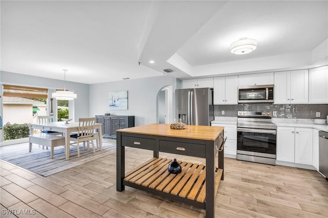 kitchen featuring stainless steel appliances, white cabinetry, hanging light fixtures, and backsplash