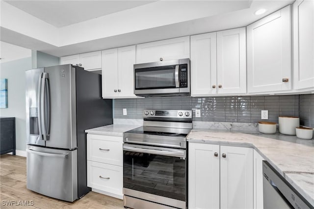 kitchen featuring stainless steel appliances, white cabinets, and light stone counters