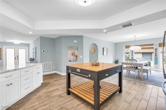 kitchen featuring white cabinetry, light wood-type flooring, pendant lighting, and light stone counters