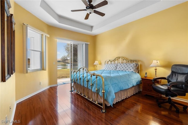 bedroom featuring dark wood-type flooring, ceiling fan, a raised ceiling, and access to outside