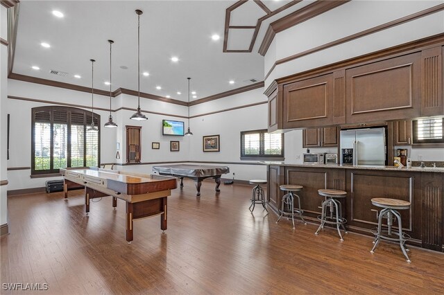 game room with dark wood-type flooring, ornamental molding, and a high ceiling