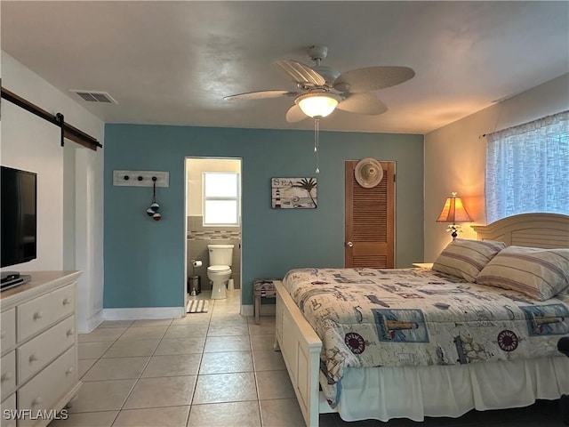 bedroom featuring a barn door, light tile patterned floors, ceiling fan, and ensuite bath