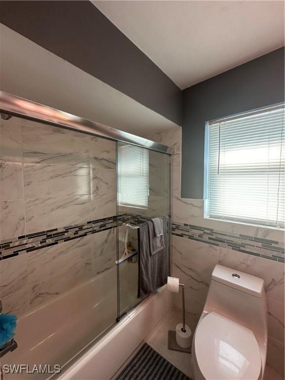 bathroom featuring tile walls, enclosed tub / shower combo, and toilet