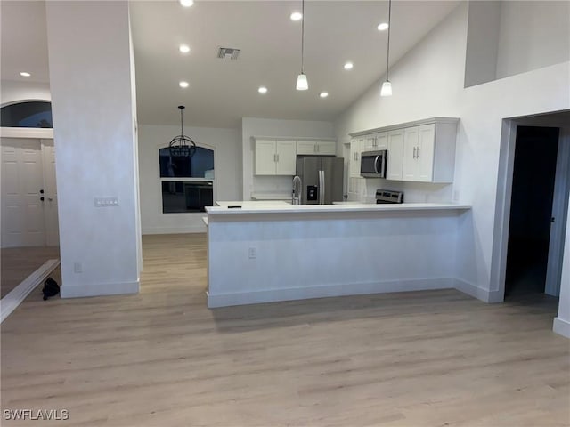 kitchen with high vaulted ceiling, decorative light fixtures, white cabinets, stainless steel appliances, and light hardwood / wood-style flooring