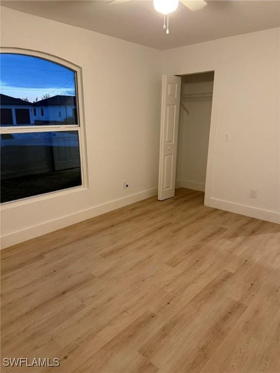 unfurnished bedroom featuring light wood-style floors, ceiling fan, baseboards, and a closet