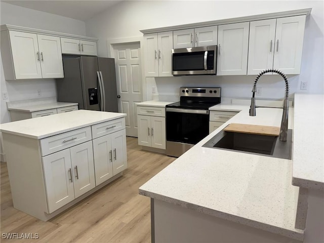 kitchen with white cabinetry, lofted ceiling, sink, stainless steel appliances, and light hardwood / wood-style flooring