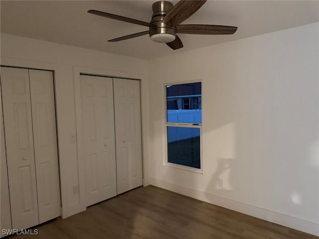 unfurnished bedroom featuring two closets, a ceiling fan, baseboards, and dark wood-type flooring