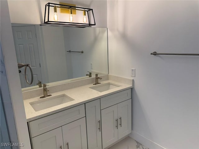 bathroom with marble finish floor, double vanity, a sink, and baseboards