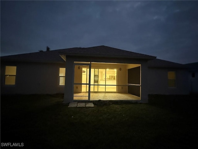 back of house at twilight with a sunroom, a patio area, and stucco siding