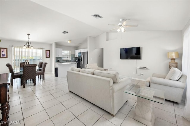 living room featuring ceiling fan with notable chandelier, vaulted ceiling, and light tile patterned floors