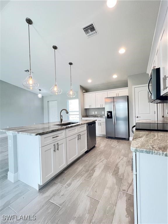 kitchen featuring appliances with stainless steel finishes, pendant lighting, white cabinetry, sink, and a kitchen island with sink