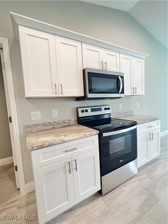 kitchen with lofted ceiling, stainless steel appliances, light stone countertops, and white cabinets