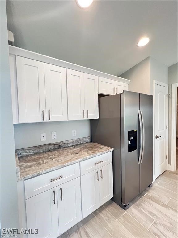 kitchen featuring white cabinets, light stone counters, and stainless steel fridge with ice dispenser