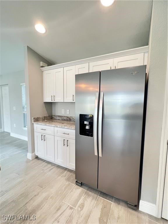 kitchen featuring white cabinets, stainless steel fridge, and light stone counters