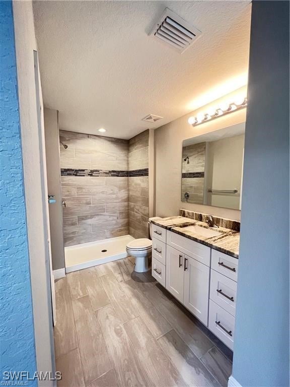 bathroom featuring vanity, toilet, a textured ceiling, and a tile shower