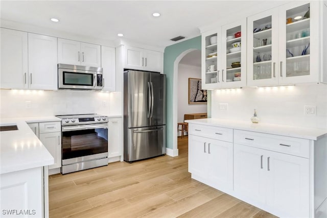 kitchen featuring tasteful backsplash, light wood-type flooring, white cabinets, and appliances with stainless steel finishes