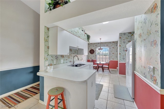 kitchen featuring sink, hanging light fixtures, light tile patterned floors, kitchen peninsula, and white cabinets