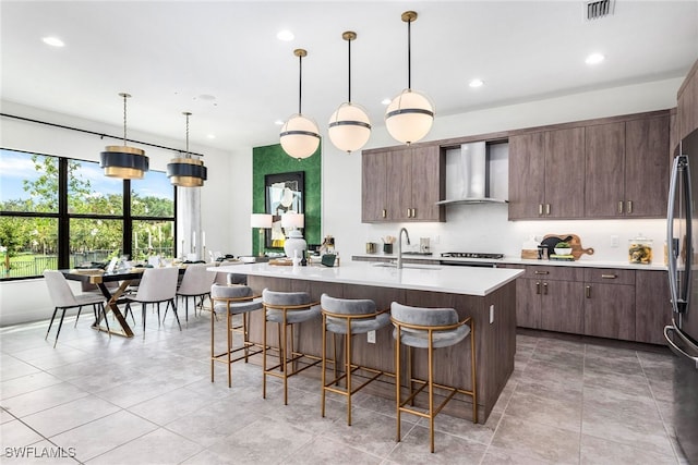 kitchen with visible vents, a breakfast bar, light countertops, wall chimney exhaust hood, and a sink