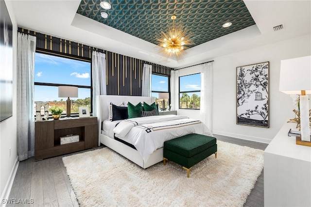 bedroom with multiple windows, baseboards, a tray ceiling, and wood finished floors