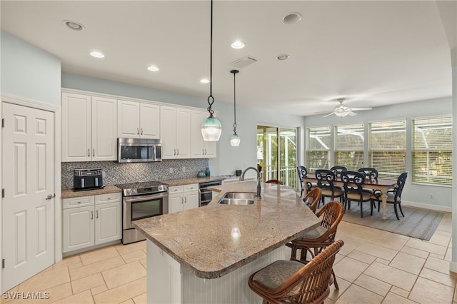 kitchen with white cabinetry, hanging light fixtures, stainless steel appliances, and a center island with sink