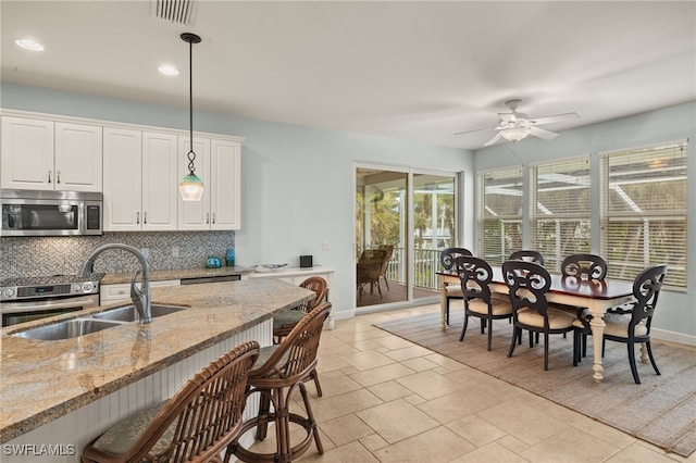 kitchen with appliances with stainless steel finishes, white cabinetry, sink, hanging light fixtures, and light stone countertops